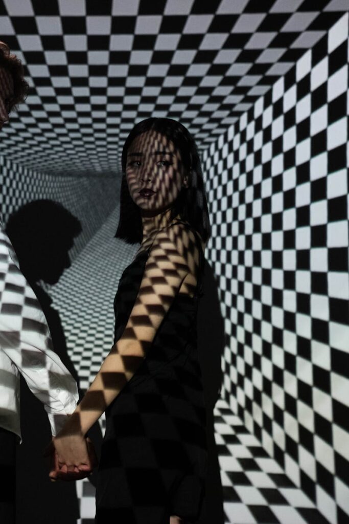 A man and woman stand in a checkered tunnel, creating a dramatic optical illusion.